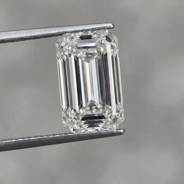 Emerald-cut diamond held by tweezers against a neutral background